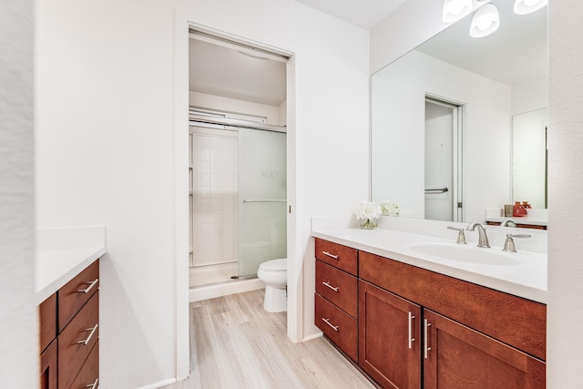 bathroom with a shower with door, vanity, hardwood / wood-style floors, and toilet