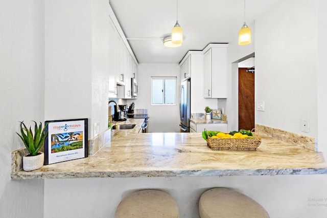 kitchen with sink, a breakfast bar area, decorative light fixtures, white cabinetry, and stainless steel appliances