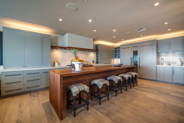 kitchen with a center island, light hardwood / wood-style flooring, paneled refrigerator, tasteful backsplash, and a kitchen bar