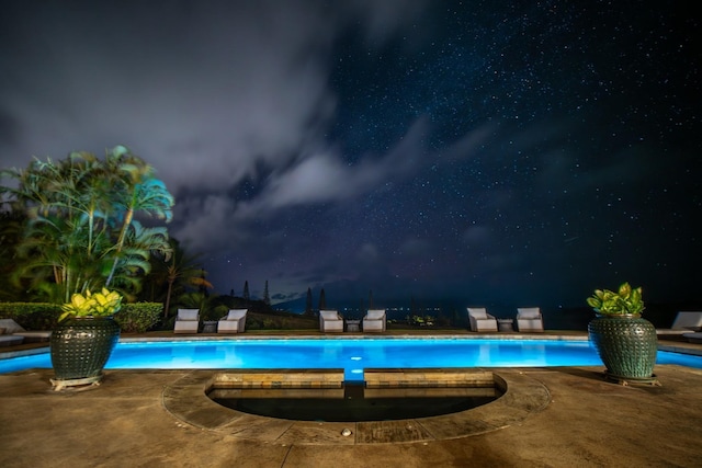 pool at night featuring a patio