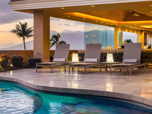 pool at dusk featuring ceiling fan, a patio, a mountain view, and an outdoor pool