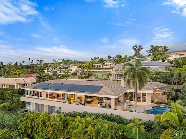 back of property with a patio, a hot tub, roof mounted solar panels, a residential view, and an outdoor pool