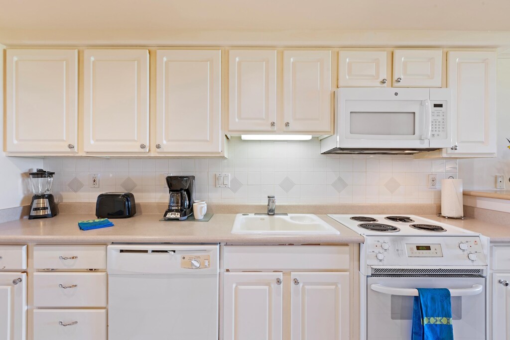 kitchen with a sink, white appliances, tasteful backsplash, and white cabinetry