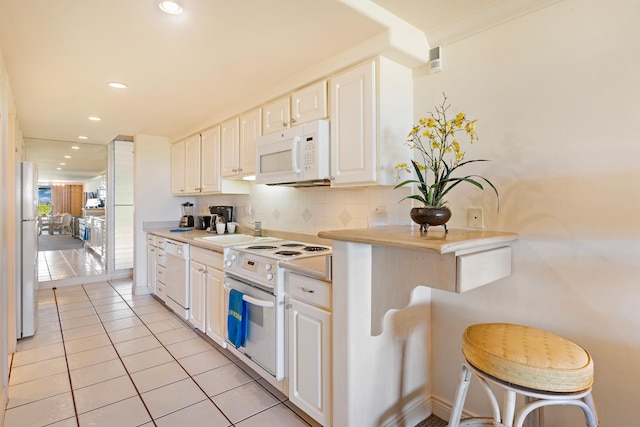 kitchen with tasteful backsplash, white cabinetry, white appliances, light tile patterned flooring, and light countertops