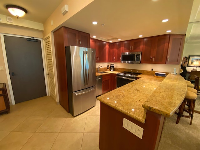 kitchen featuring light stone counters, stainless steel appliances, sink, light tile patterned flooring, and a breakfast bar area