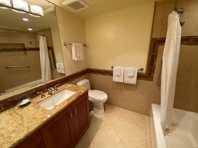 full bathroom with tile patterned floors, toilet, tile walls, shower / tub combo with curtain, and vanity