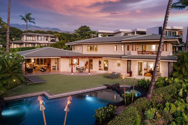 back house at dusk featuring a patio and a yard