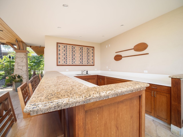 kitchen featuring light tile patterned flooring, light stone counters, sink, and kitchen peninsula