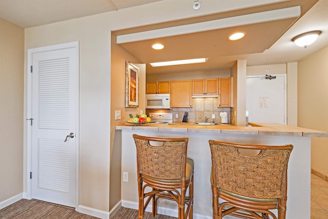 4327 Lower Honoapiilani Rd Unit 1002B, Lahaina, HI 96761 - kitchen featuring white microwave, range, a kitchen bar, baseboards, and decorative backsplash