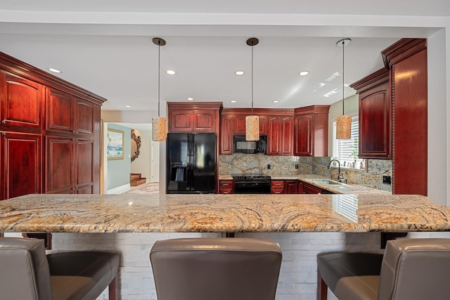 kitchen with a kitchen bar, black appliances, reddish brown cabinets, and a sink