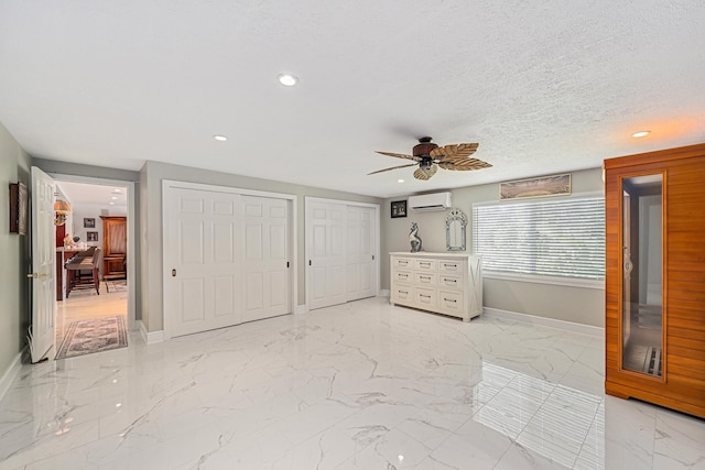 unfurnished bedroom featuring baseboards, multiple closets, an AC wall unit, marble finish floor, and a textured ceiling