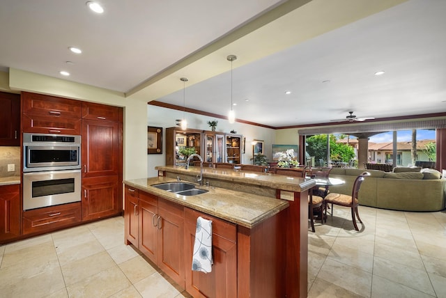 kitchen featuring ceiling fan, sink, light stone countertops, double oven, and decorative light fixtures