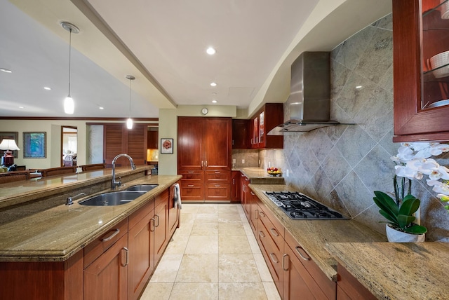 kitchen featuring light stone counters, gas stovetop, sink, wall chimney range hood, and pendant lighting