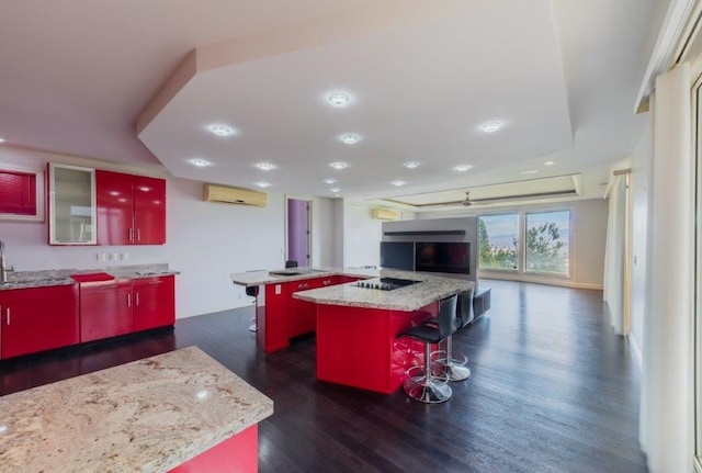 kitchen featuring a center island, a kitchen breakfast bar, an AC wall unit, light stone counters, and dark hardwood / wood-style flooring