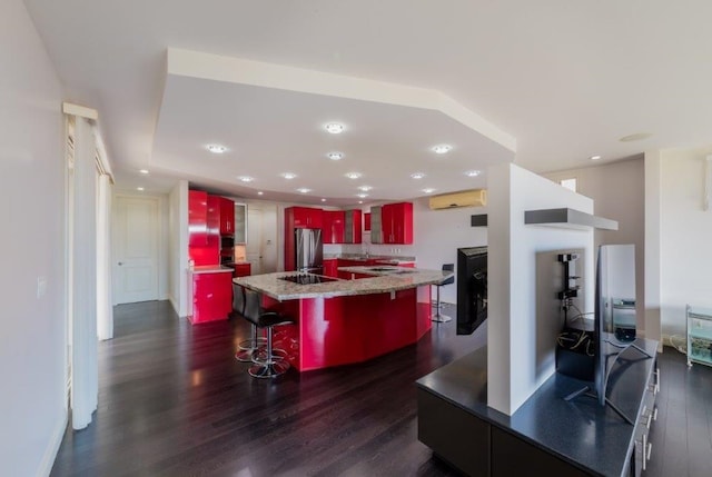 kitchen featuring a kitchen breakfast bar, light stone countertops, an island with sink, dark hardwood / wood-style flooring, and stainless steel refrigerator