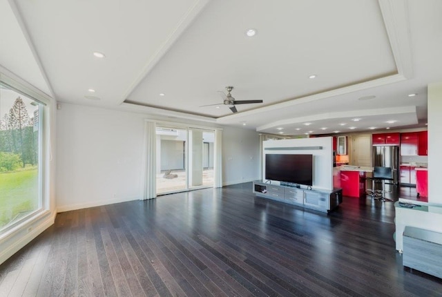 unfurnished living room featuring a tray ceiling, ceiling fan, and dark hardwood / wood-style flooring