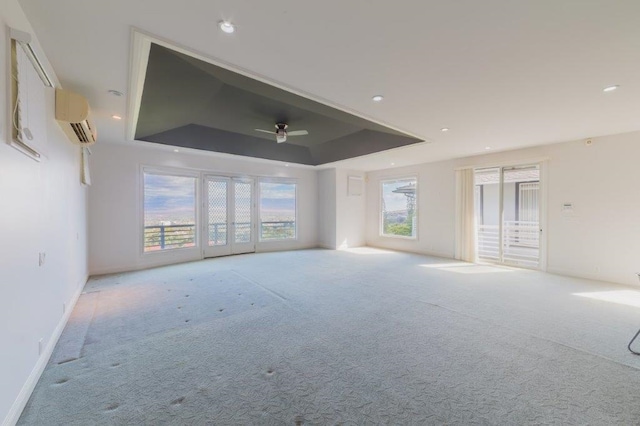 unfurnished living room with a wall mounted air conditioner, light colored carpet, a raised ceiling, and ceiling fan