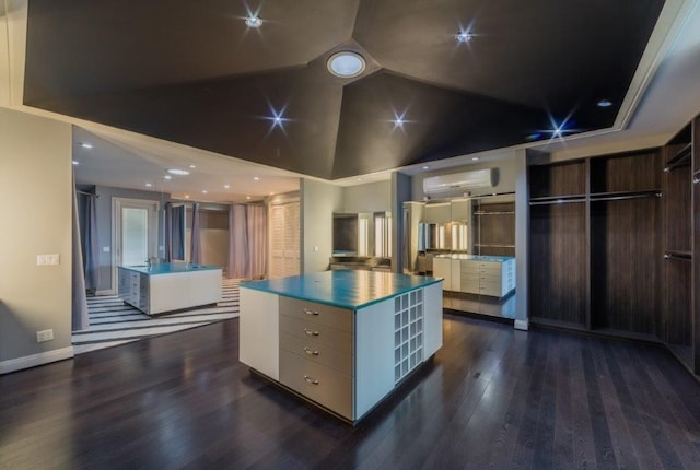 kitchen with a wall mounted air conditioner, dark wood-type flooring, a spacious island, high vaulted ceiling, and white cabinets