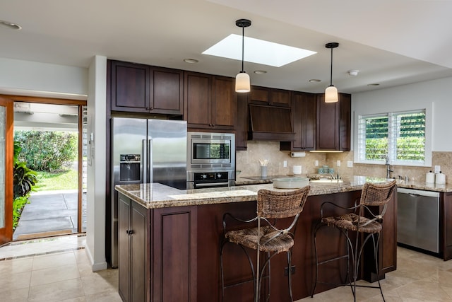 kitchen featuring custom exhaust hood, hanging light fixtures, a skylight, decorative backsplash, and appliances with stainless steel finishes