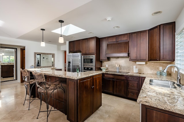 kitchen featuring a skylight, stainless steel appliances, sink, decorative light fixtures, and a center island