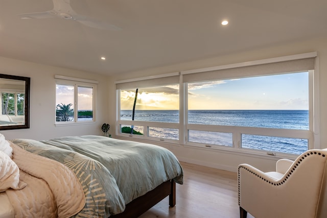 bedroom with ceiling fan, light hardwood / wood-style flooring, a water view, and a beach view