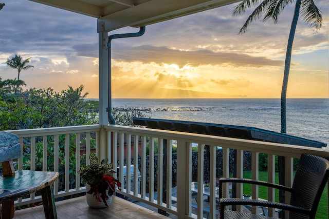 balcony at dusk with a water view and a view of the beach