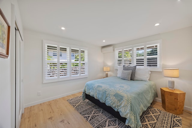 bedroom featuring an AC wall unit, multiple windows, and light hardwood / wood-style floors