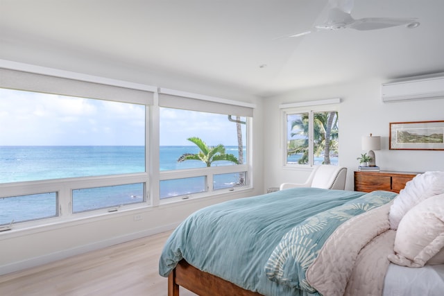 bedroom with ceiling fan, a water view, light hardwood / wood-style flooring, and a wall mounted AC