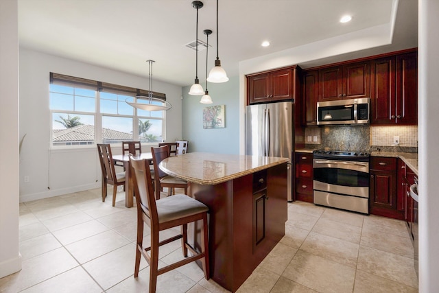 kitchen featuring pendant lighting, a center island, tasteful backsplash, light tile patterned floors, and stainless steel appliances