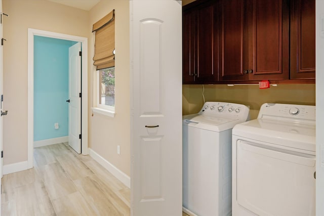 laundry room featuring baseboards, light wood-type flooring, cabinet space, and washing machine and clothes dryer
