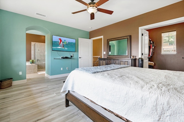 bedroom with visible vents, baseboards, light wood-type flooring, connected bathroom, and arched walkways