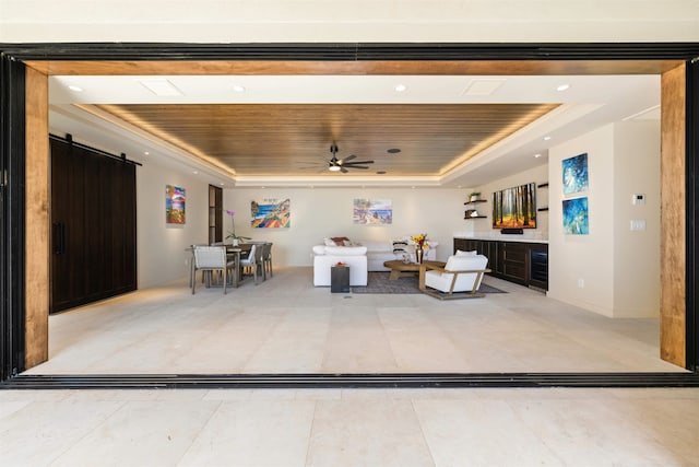 living room with a barn door, a tray ceiling, ceiling fan, and wooden ceiling