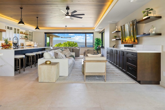 living room featuring ceiling fan, wood ceiling, sink, and a tray ceiling