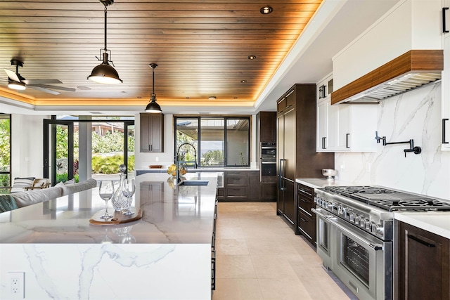 kitchen featuring light stone counters, custom range hood, dark brown cabinetry, decorative light fixtures, and range with two ovens