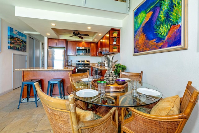 tiled dining space featuring ceiling fan and a raised ceiling