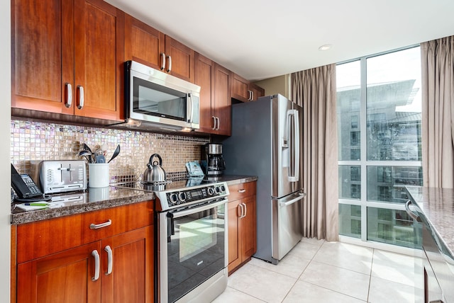 kitchen featuring stainless steel appliances, dark stone counters, tasteful backsplash, and light tile patterned floors