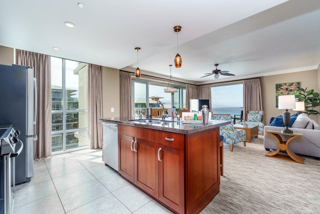 kitchen with appliances with stainless steel finishes, hanging light fixtures, an island with sink, dark stone countertops, and ceiling fan