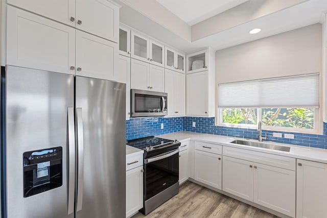 kitchen with white cabinets, sink, appliances with stainless steel finishes, tasteful backsplash, and light hardwood / wood-style floors