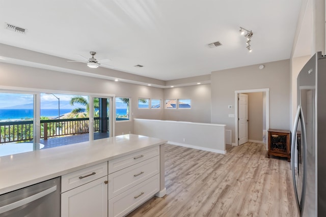 kitchen featuring appliances with stainless steel finishes, light wood-type flooring, ceiling fan, a water view, and white cabinetry