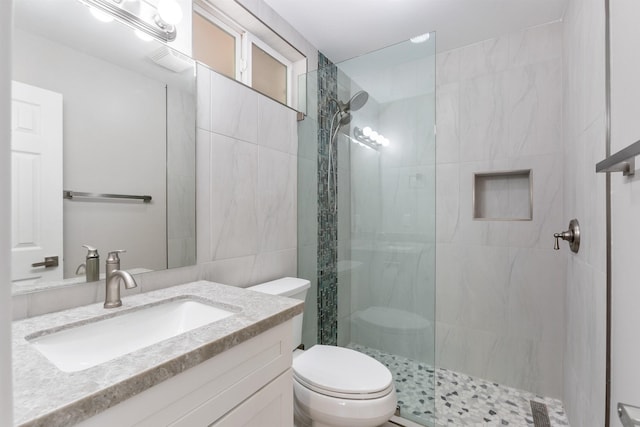 bathroom with a tile shower, vanity, tile walls, and toilet