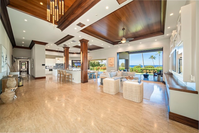 living room featuring ceiling fan, a raised ceiling, and decorative columns