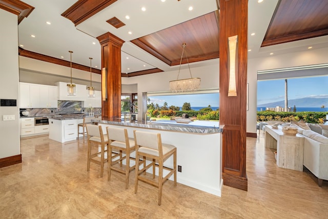 kitchen with ornate columns, a kitchen breakfast bar, a notable chandelier, decorative light fixtures, and white cabinets