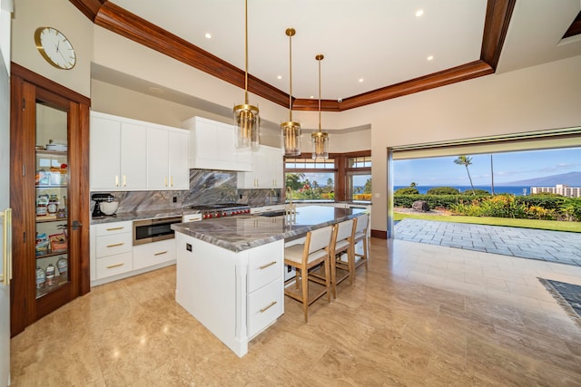 kitchen with white cabinets, pendant lighting, a center island with sink, and dark stone counters