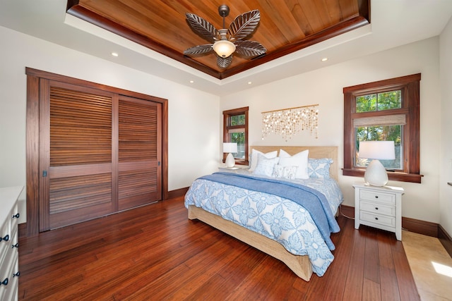 bedroom with hardwood / wood-style floors, wooden ceiling, a raised ceiling, ceiling fan, and a closet