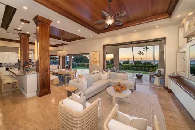 living room featuring ceiling fan with notable chandelier, a raised ceiling, ornate columns, ornamental molding, and wood ceiling