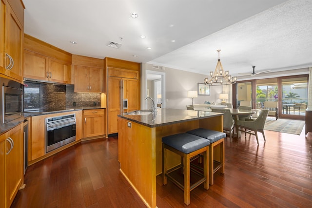 kitchen featuring a kitchen breakfast bar, ceiling fan with notable chandelier, sink, built in appliances, and an island with sink