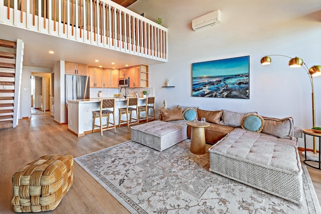 living room with a high ceiling, light hardwood / wood-style floors, a wall mounted AC, and sink