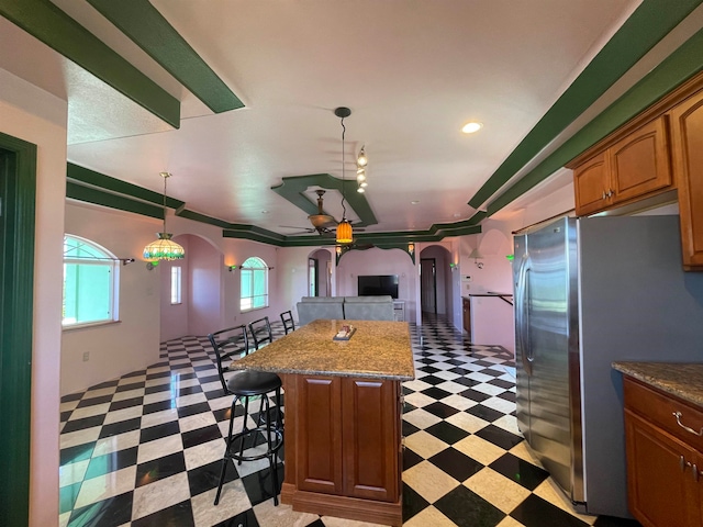 kitchen featuring a center island, a kitchen breakfast bar, hanging light fixtures, stainless steel fridge, and ornamental molding