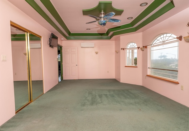 interior space with carpet, a tray ceiling, an AC wall unit, and ceiling fan