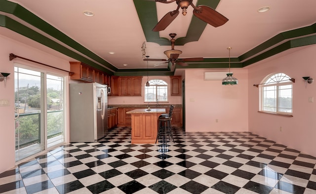 kitchen with ceiling fan, hanging light fixtures, a kitchen breakfast bar, stainless steel fridge, and a kitchen island